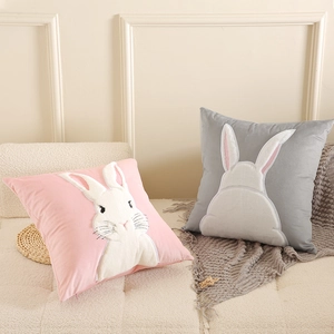 Pink and grey velvet rabbit throw pillows with embroidered bunny designs on a soft sofa