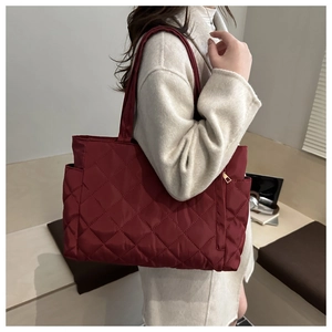 Detail of burgundy quilted tote bag with diamond pattern and gold zipper on the side