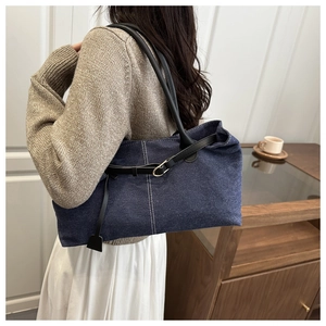 Dettaglio della borsa tote in denim blu scuro con manici in pelle nera e cuciture bianche