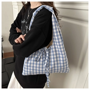 Detail of blue and white gingham tote bag featuring a decorative side bow on a soft fabric