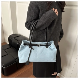 Detail of light blue tote bag featuring black slim straps and gold buckle accent