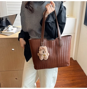 Detail of a brown woven tote bag with a small plush bear charm for daily commuting