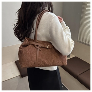 Detail showing brown corduroy tote texture with vintage leather strap and gold buckle