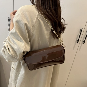 Brown patent leather saddle bag with gold chain strap shown on beige trench coat