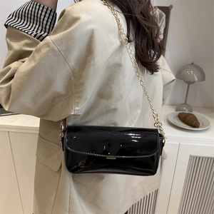 Glossy black patent leather saddle bag with gold chain strap on a model for daily use