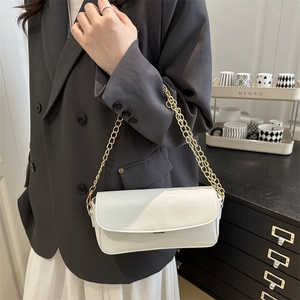 White patent leather saddle bag with gold chunky chain strap worn over grey blazer