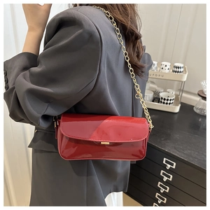 Red glossy saddle bag with gold chain strap shown on a gray blazer for a minimalist look