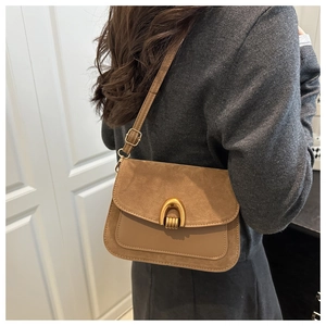 Detail of brown suede crossbody bag with golden horseshoe buckle on white background
