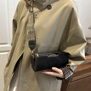 Borsa a tracolla cilindrica nera con tracolla boho indossata su un cappotto kaki