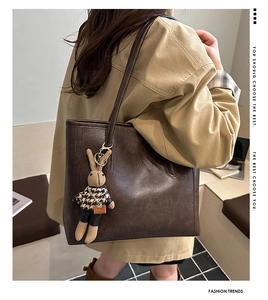 Detail view of large dark brown leather tote bag with a beige long-eared rabbit charm