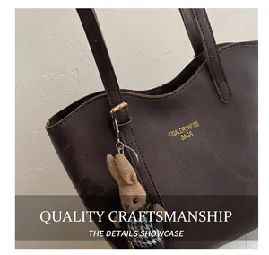 Detail of dark brown tote bag with leather texture, brand logo and plush rabbit pendant