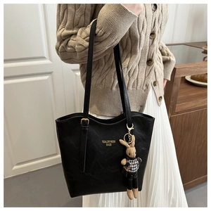 Detail of black leather tote bag with gold logo and houndstooth rabbit doll charm