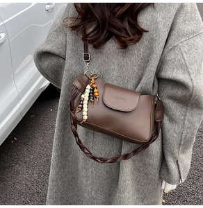 Detail shot of a brown leather crescent bag with wooden bead charm and woven shoulder strap