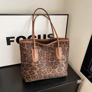 Close-up of leopard print tote bag with brown leather handles on wooden surface