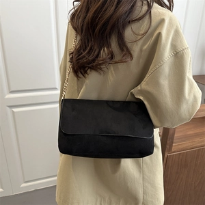 Borsa a tracolla rettangolare nera con catena dorata indossata su cappotto beige