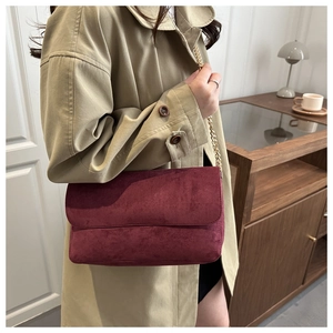 Detail of burgundy suede shoulder bag with gold chain strap worn over a beige coat
