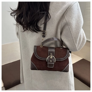 Detail of vintage brown suede crossbody bag with a large gold buckle and white stitching