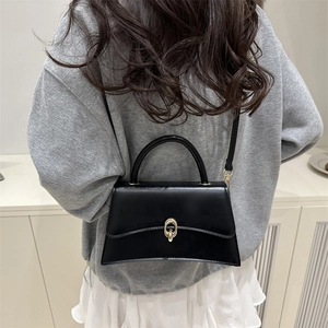 Classic black leather crossbody bag with golden ring buckle shown on a model