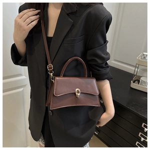 Close-up of a minimalist dark brown leather crossbody bag with vintage gold hardware