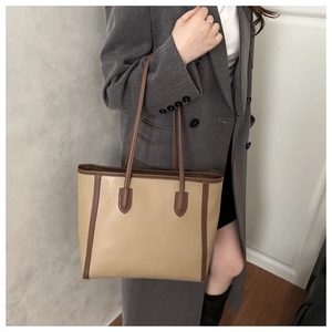 Close-up of large beige leather tote bag with dark brown straps and reinforced stitching