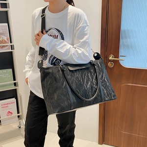 Large black pleated travel tote bag with shoulder strap shown in a home setting