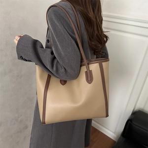 Large beige and brown two-tone leather tote bag worn by a model in a minimal setting