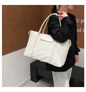 Detailed side view of a large white travel tote bag worn by a model in a warm room