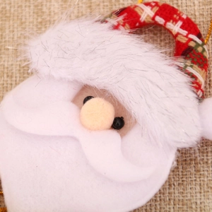 Close-up of Santa plush ornament with red plaid hat and bell on burlap background