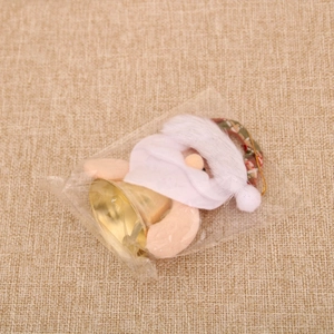 Détail d'un ornement du Père Noël en peluche avec cloche dorée sous emballage