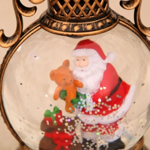 Detalle de farol navideño de bronce vintage con Papá Noel en su interior y luz cálida