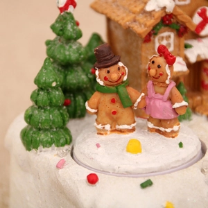 Détail d'un couple en pain d'épices sur socle enneigé avec maison de Noël