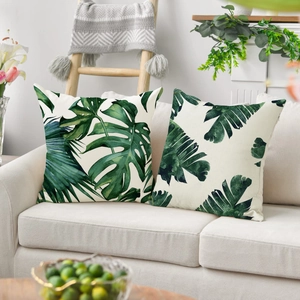 Tropical monstera and palm leaf print throw pillow covers on a beige fabric sofa