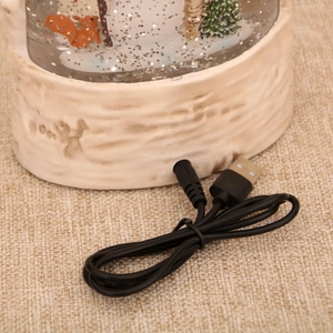 Detail of white faux wood base with USB charging port for squirrel snow globe music box