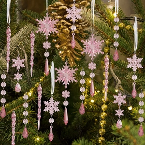 Pink acrylic icicle and snowflake ornaments hanging on a Christmas tree with festive lights