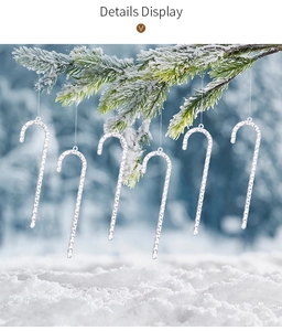 Detailed view of six clear acrylic candy cane ornaments hanging on a snowy pine branch