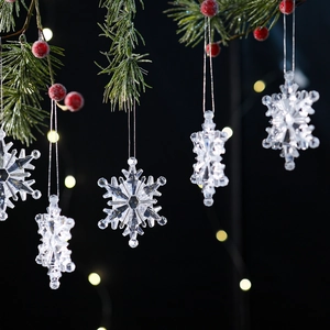 Transparent acrylic snowflake ornaments hanging on pine branches with warm bokeh lights