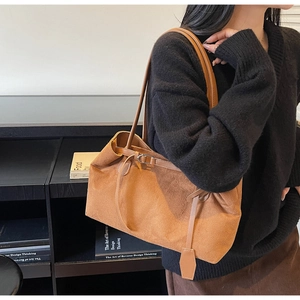 Detail view of a large brown suede tote bag with slim straps worn by a model in a minimal setting