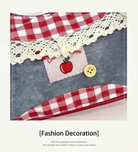 Detail of blue denim pet bib with apple patch, red plaid trim and white lace edges