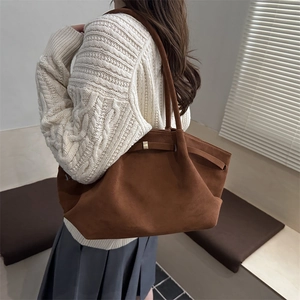 Brown suede tote bag with gold metal buckles shown on shoulder with a white knit sweater