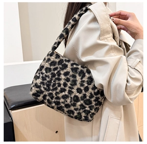 Leopard print plush shoulder bag shown on shoulder over a beige coat in home setting