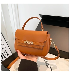 Detail of caramel brown handbag featuring gold twist lock and smooth leather texture