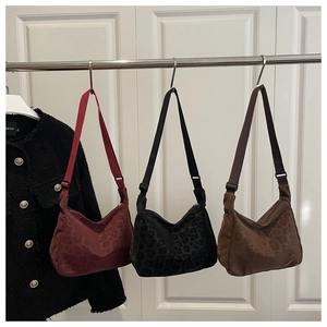 Three leopard print tote bags in burgundy, black and brown hanging on metal hooks