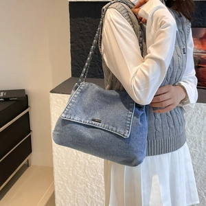 Blaue Denim-Tragetasche mit Kettenriemen getragen von Modell in modernem Outfit