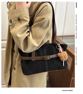 Detail view of black canvas tote bag with brown leather straps and plush bear charm