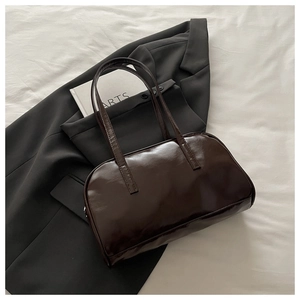 Detalle de bolso de hombro marrón oscuro brillante sobre traje grisáceo