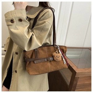 Detail of vintage brown suede tote bag with leather strap and plush bear charm on a model