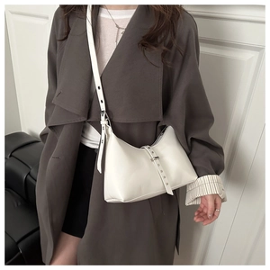 Dettaglio della borsa bianca minimalista con tracolla regolabile su cappotto grigio