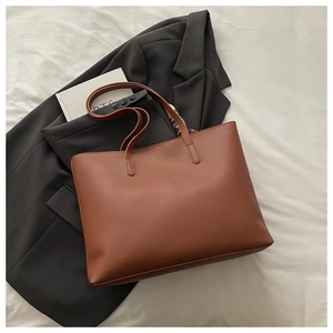 Détail d'un grand sac cabas marron sur des draps blancs avec une veste pour un style chic
