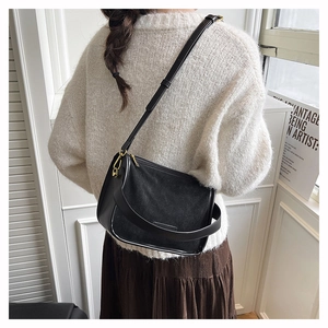 Gros plan sur un sac à bandoulière en daim et cuir noir avec boucles métalliques dorées