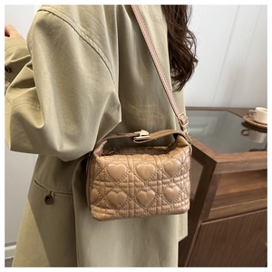 Detail of khaki heart-quilted bucket bag with metal clasp worn by a model